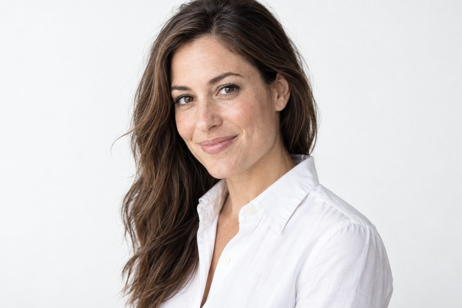 A studio headshot in a white shirt against a bone-white wall
