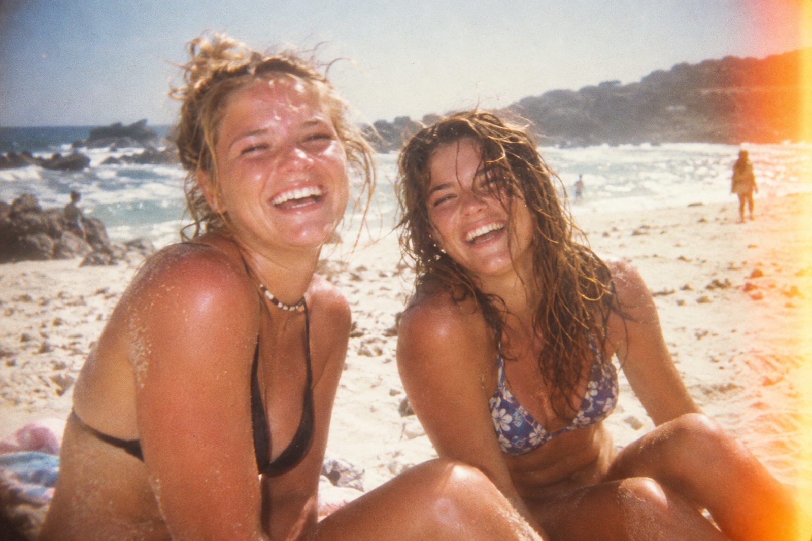 Two friends laughing on a sunlit beach, shot on film